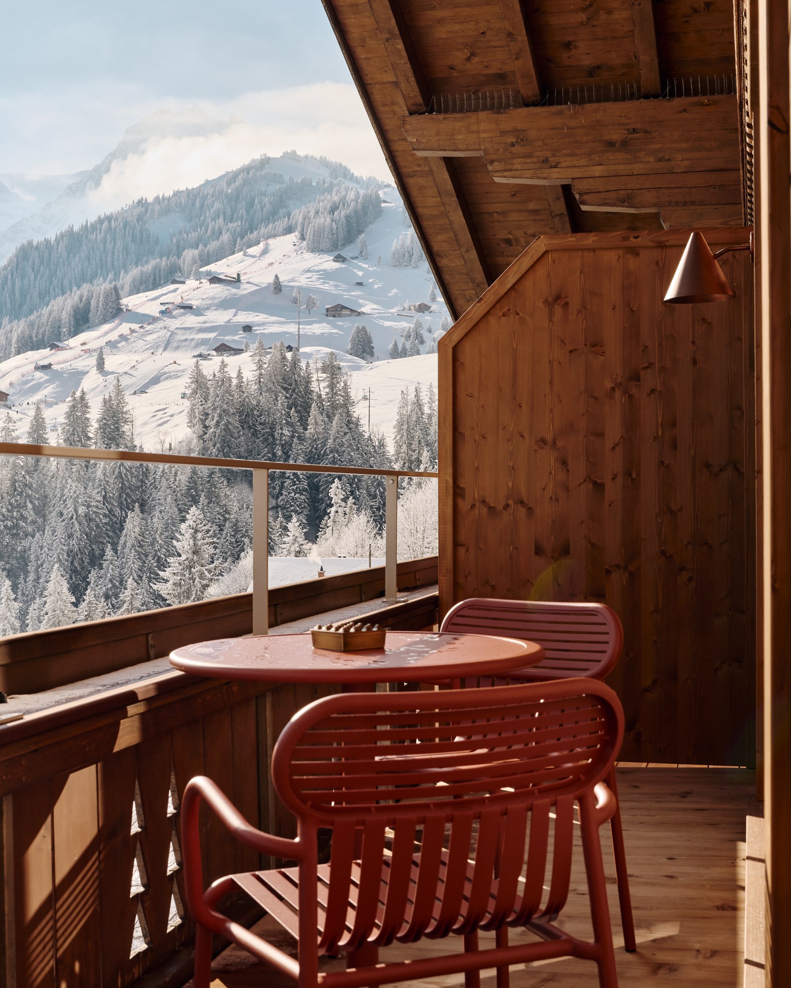 A red table and chairs on a snowy balcony overlooking Adelboden.